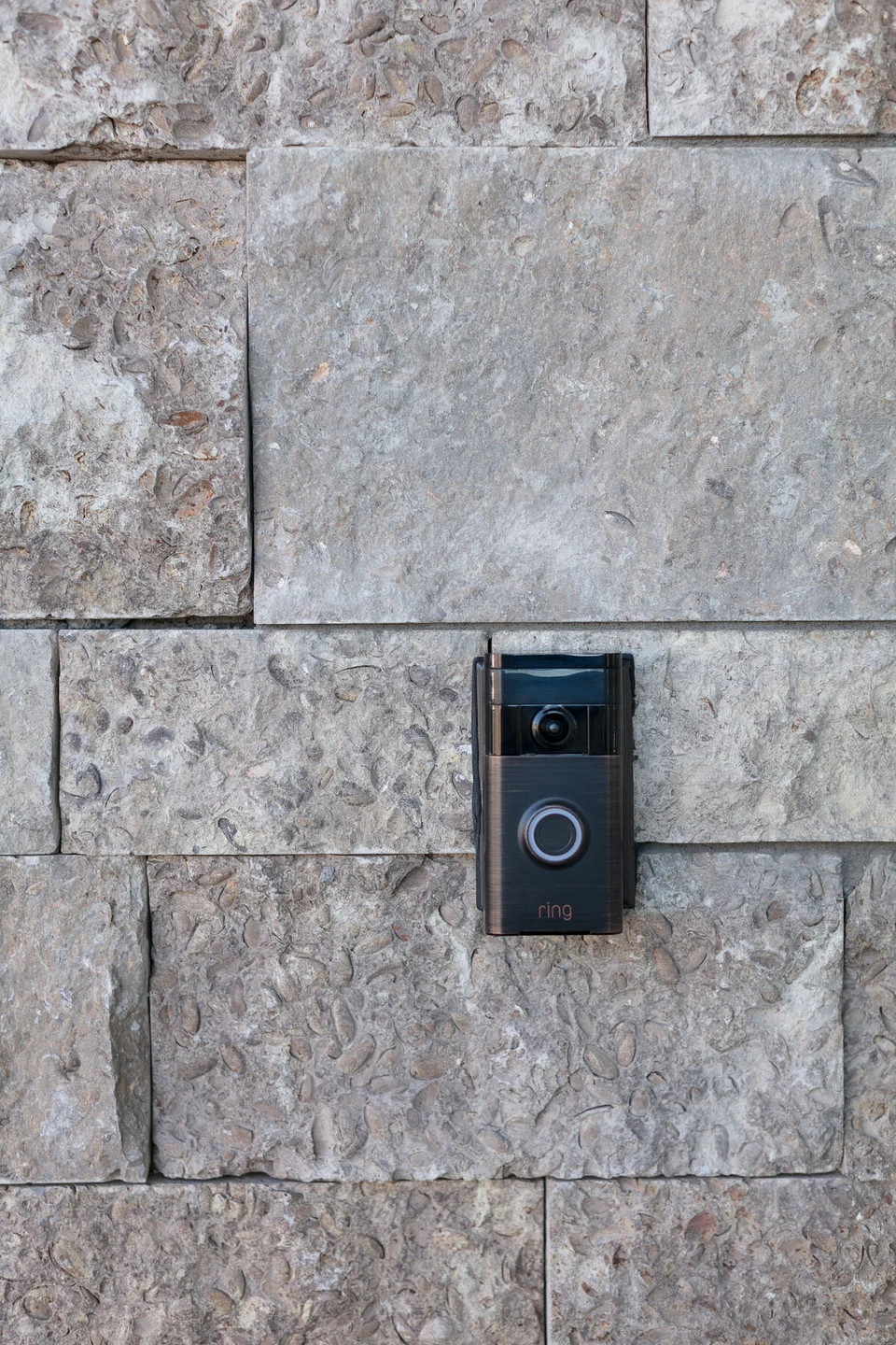 Black video doorbell mounted beside the stone entryway