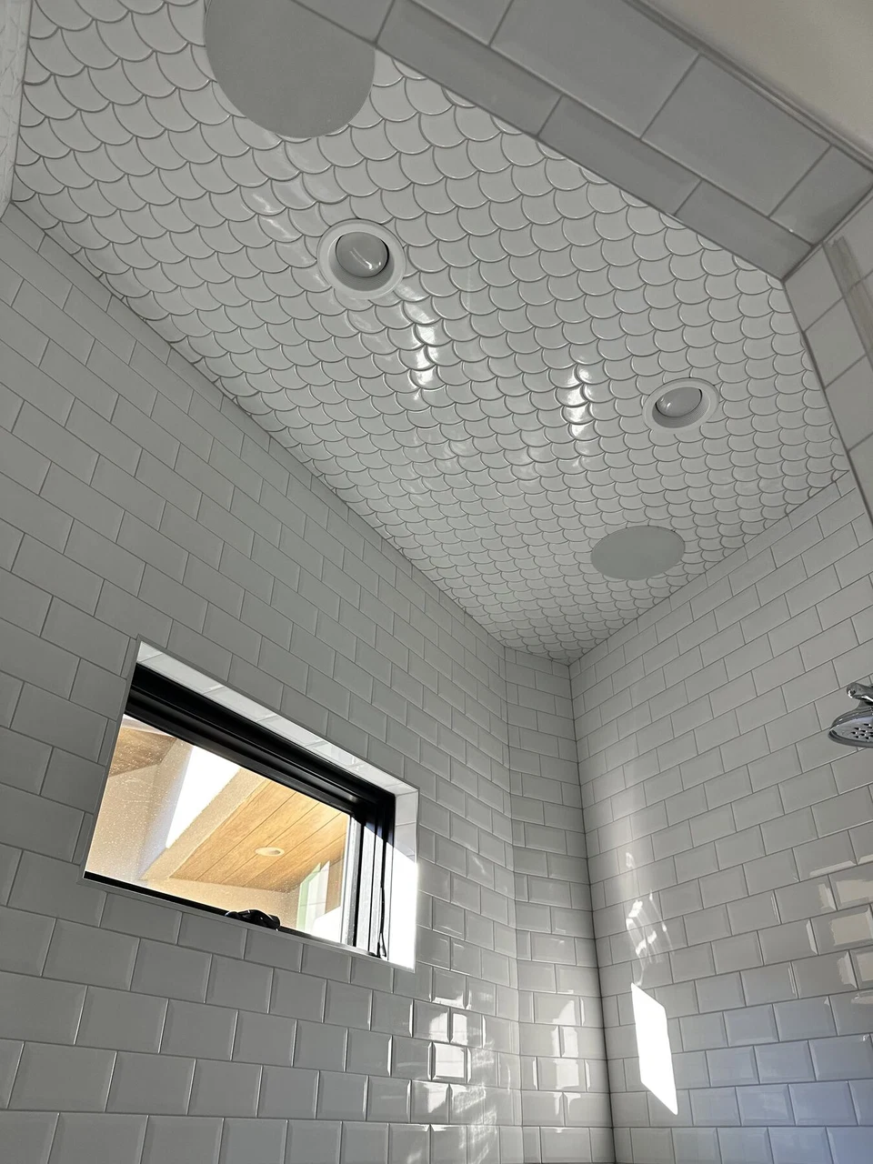 Tiled shower ceiling with recessed light, round speaker, and showerhead