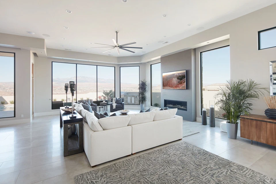 White living room sofas facing a television and fireplace beside tall windows