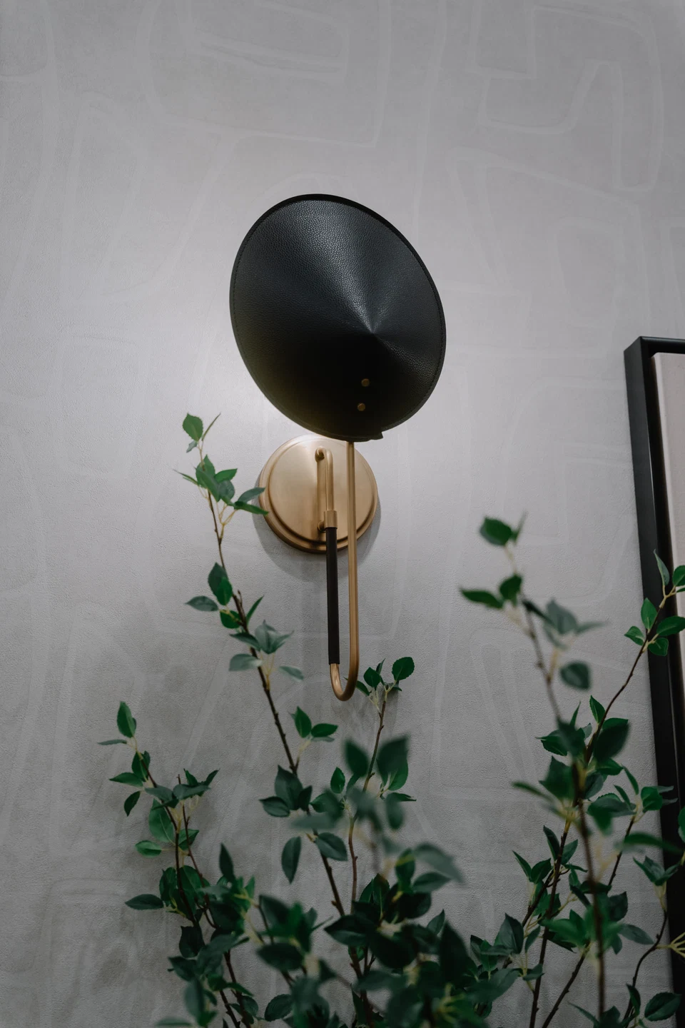 Round black-and-brass wall sconce above a leafy plant