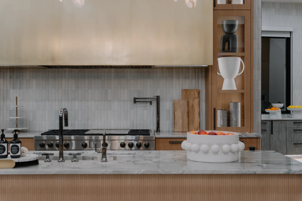 Kitchen island facing a range, stone backsplash, and illuminated wood shelving