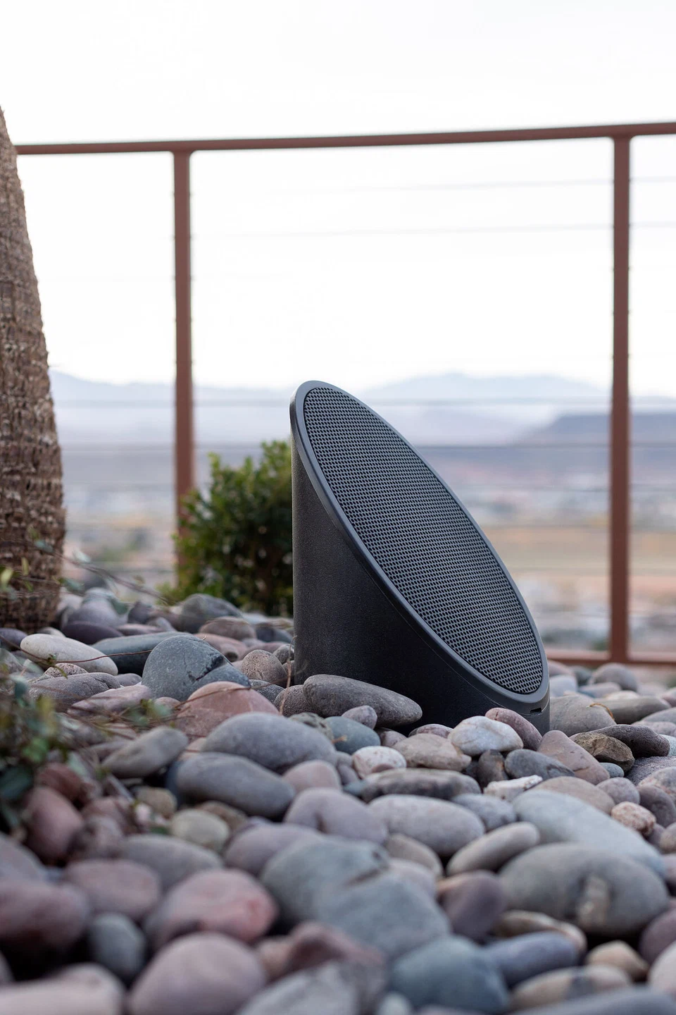 Small dark landscape speaker angled upward in a gravel bed