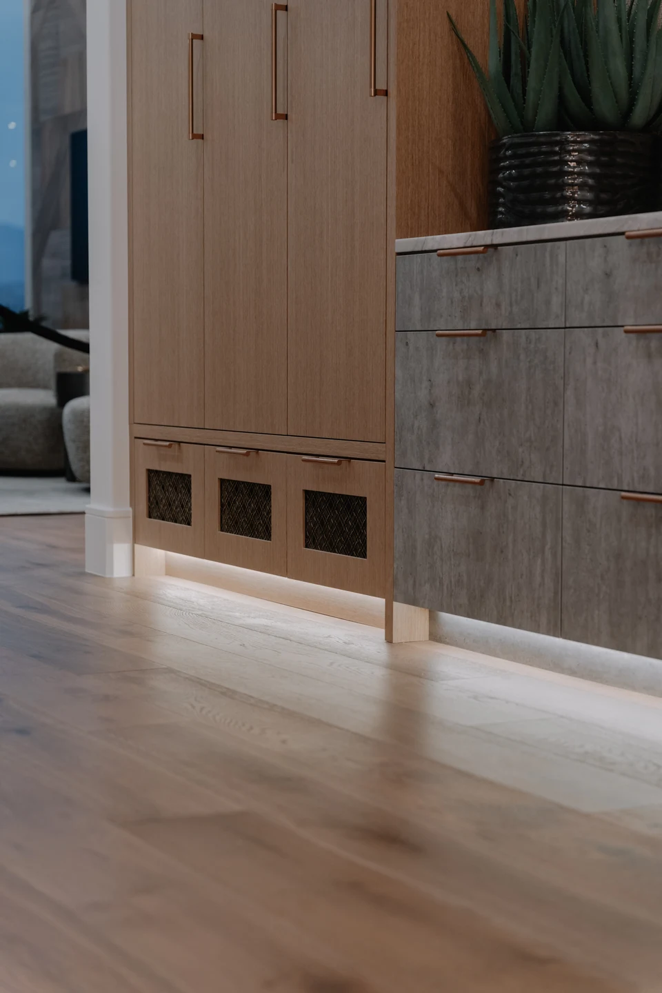 Floor-level lighting beneath wood cabinetry and a stone countertop