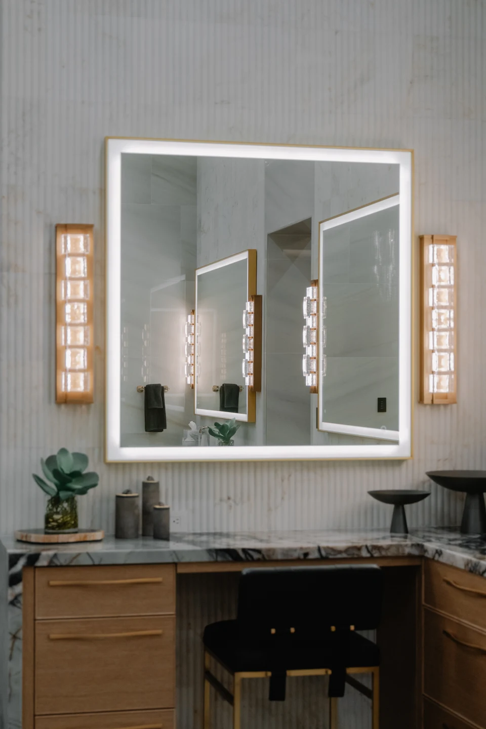 Bathroom vanity with a large illuminated mirror and paired wall sconces
