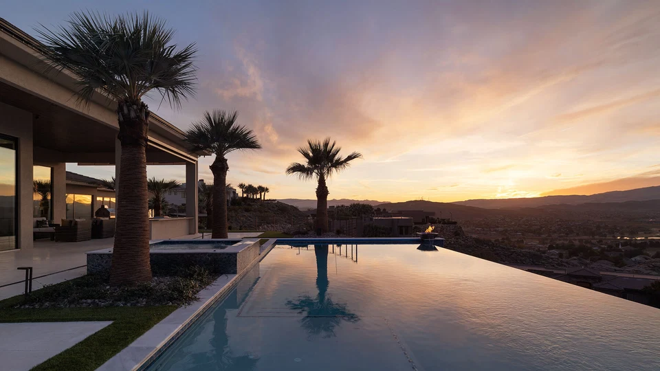 Infinity pool reflecting palm trees and a colorful sunset beside the home