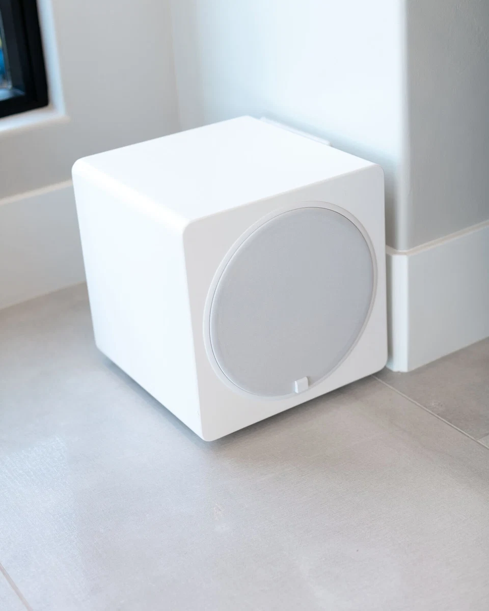 Compact white subwoofer on tile flooring beside a window