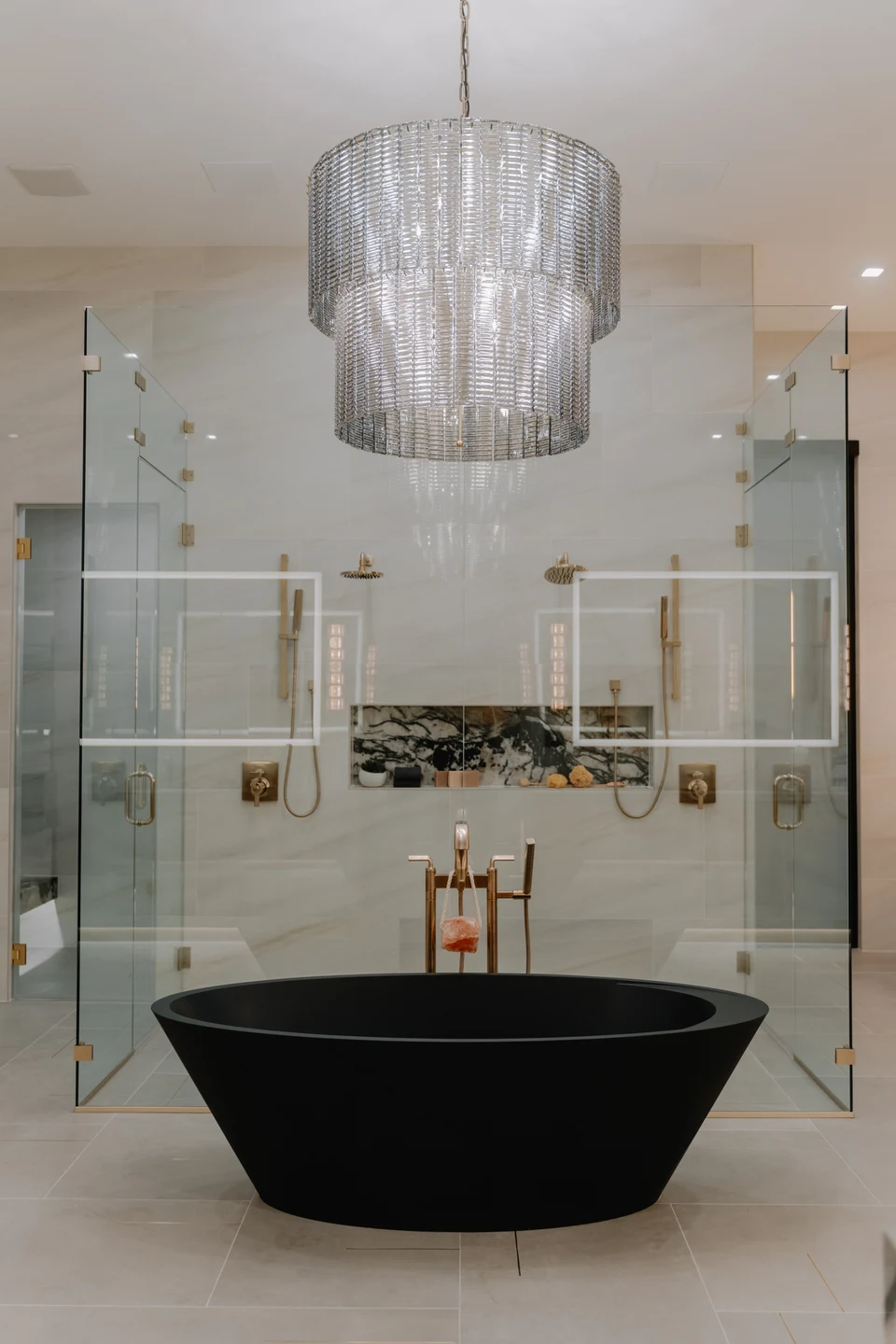 Black freestanding bathtub beneath a chandelier in a marble bathroom