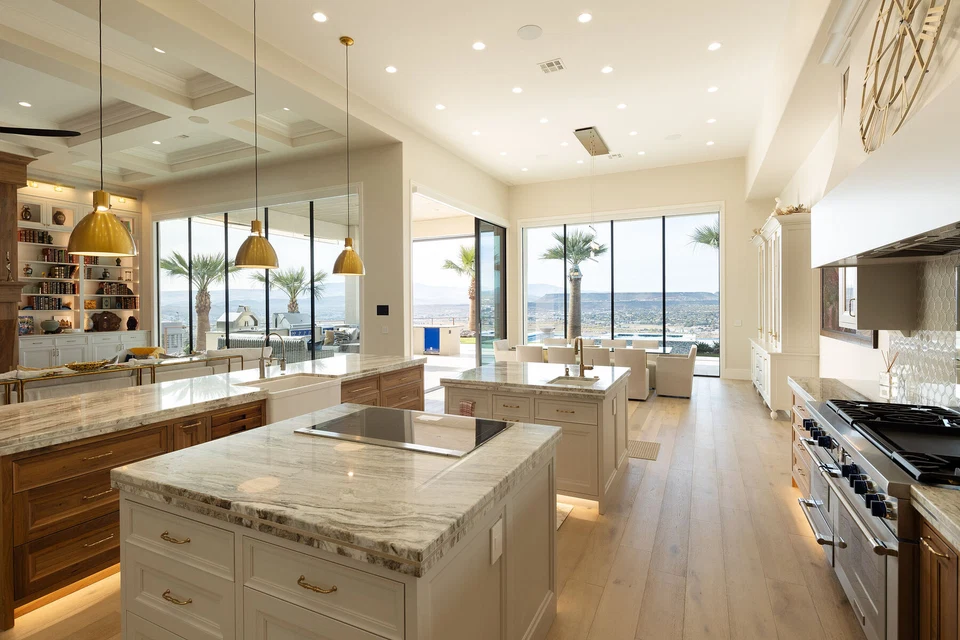 Long kitchen island beneath recessed ceiling lights beside glass patio doors