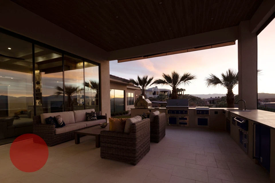 Covered outdoor seating and kitchen beside glass doors at dusk