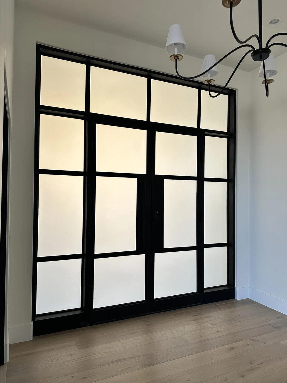 Black-framed frosted glass interior doors beneath a chandelier