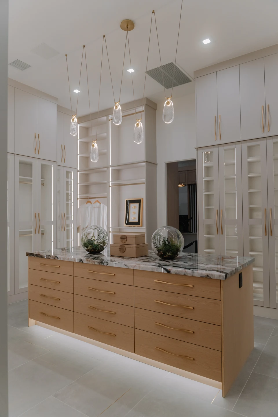 Long bathroom vanity beneath hanging glass pendants and recessed ceiling lights