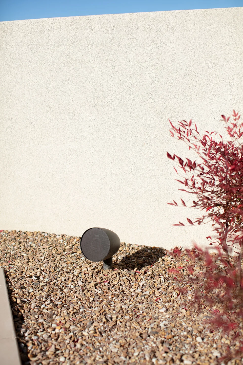 Rock-shaped landscape speaker among gravel and red shrubs