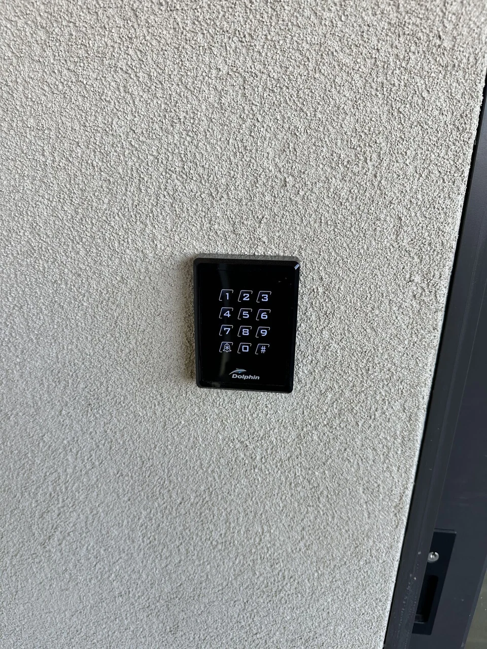 Black multi-button control keypad on an exterior stucco wall