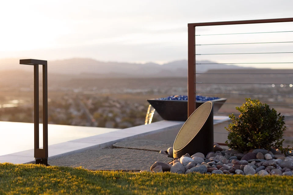Outdoor landscape speaker beside a poolside path and metal railing