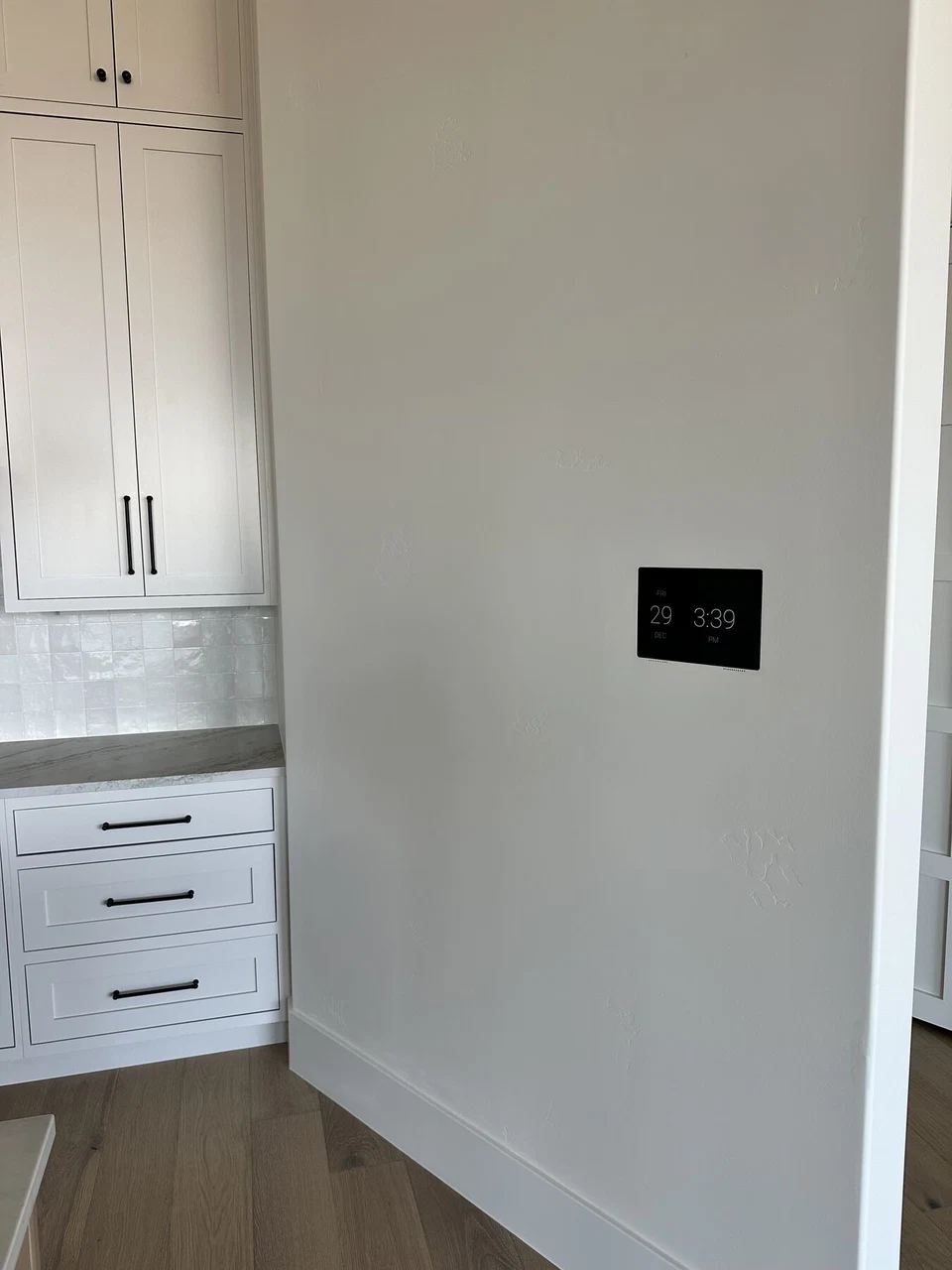 Black wall keypad beside white kitchen cabinetry before furnishing