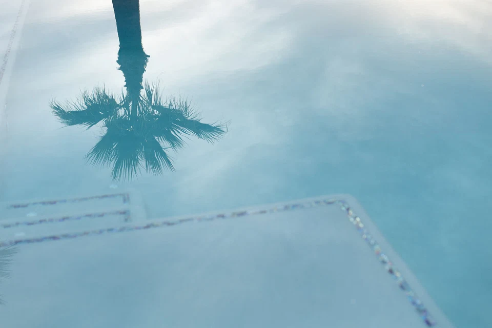 Palm tree reflection on pale blue pool water above submerged steps