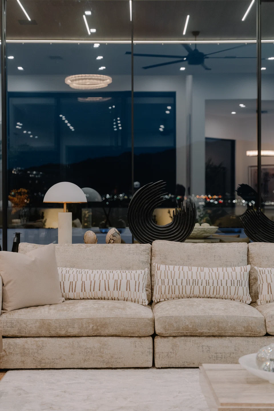 Living room sofa and pendant lights reflected in tall windows after dark