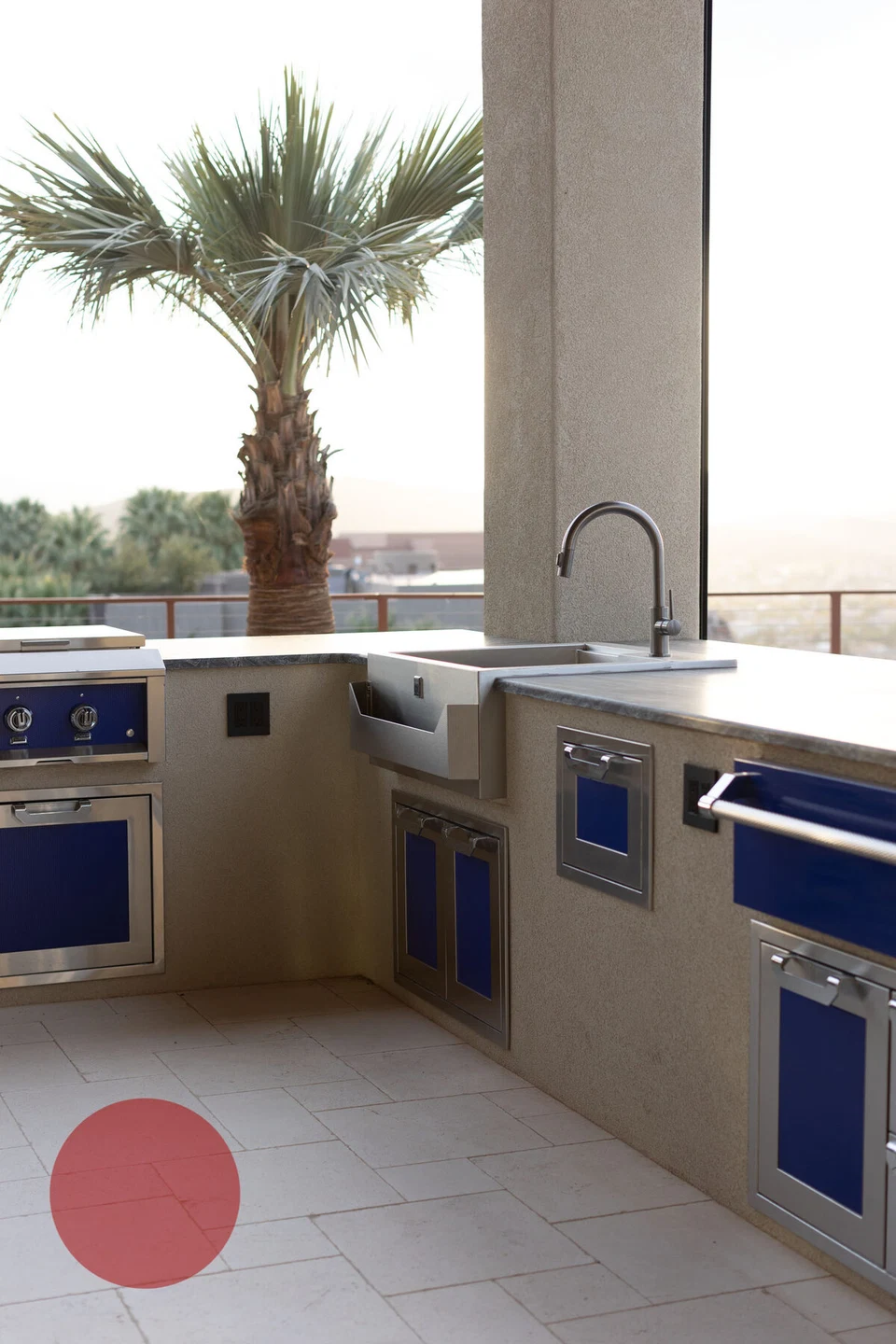 Outdoor kitchen counter with built-in grill beside a palm-lined pool