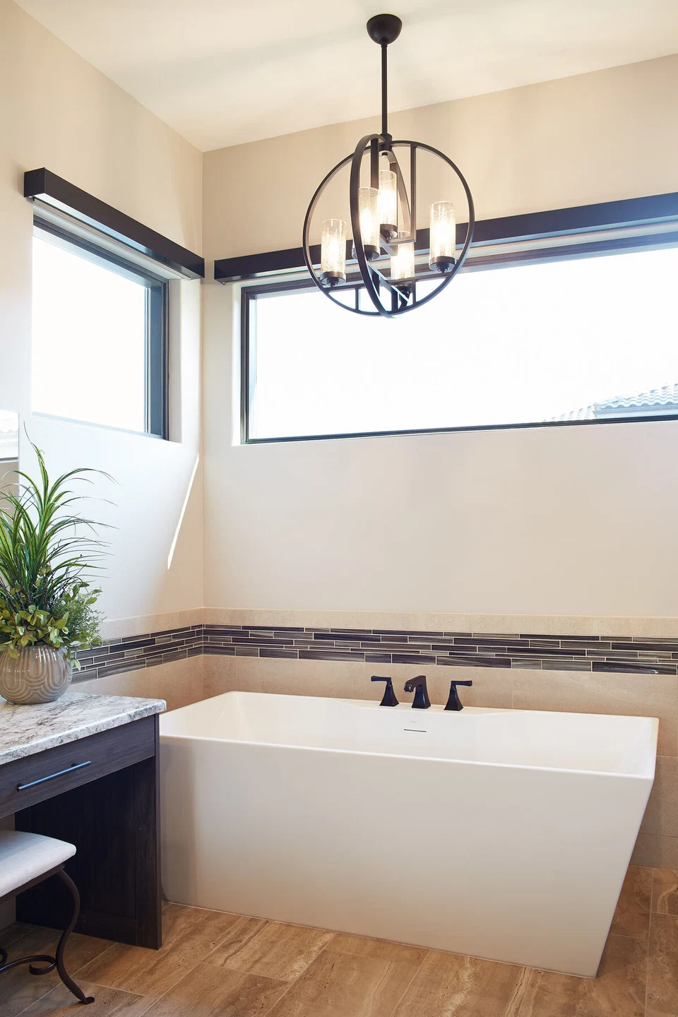 White bathtub beneath corner windows and a hanging light fixture