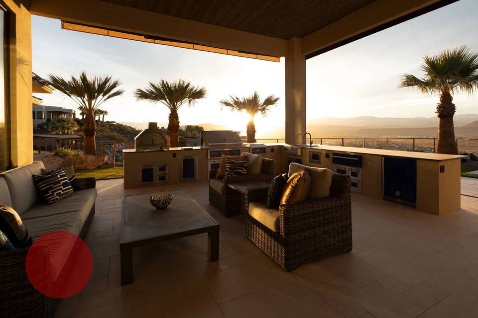Covered patio lounge and outdoor kitchen overlooking palm trees at sunset