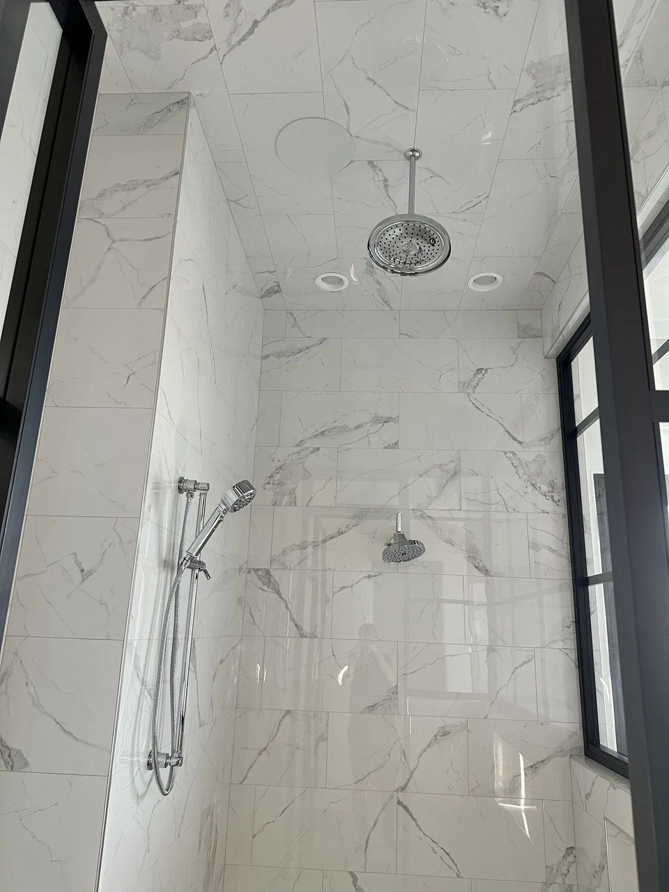 Glass-enclosed marble shower with rainfall head and handheld sprayer