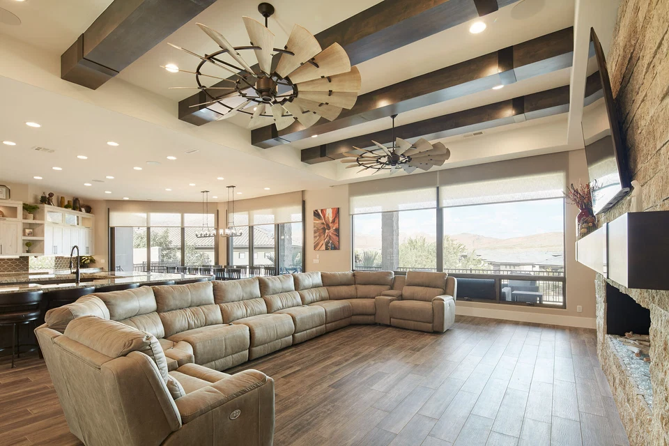 Living room seating beside broad windows and a stone fireplace wall