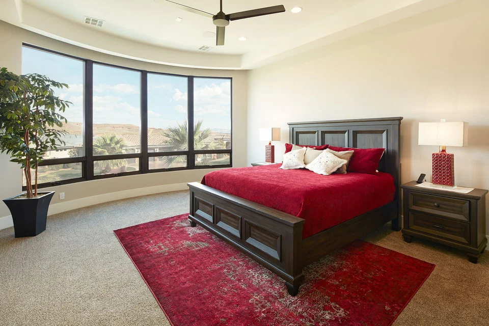 Bedroom with red bedding and rug beneath a large ceiling fan