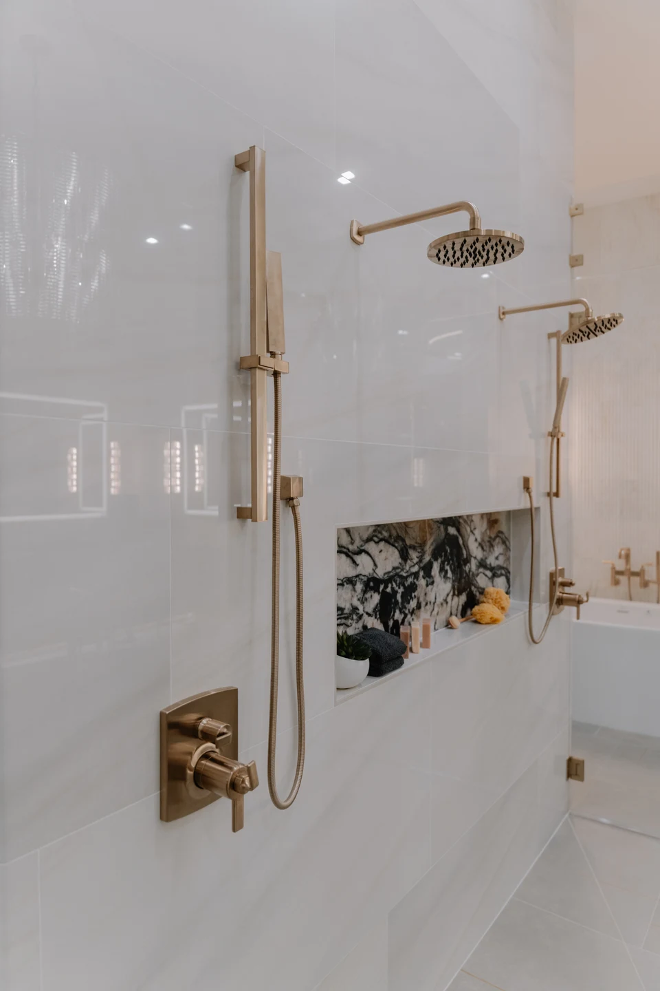 Brass shower controls and showerhead against pale marble tile