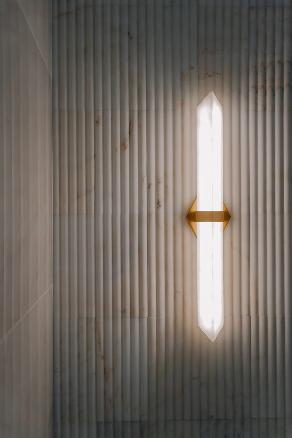 Vertical wall light with brass trim on dark fluted paneling