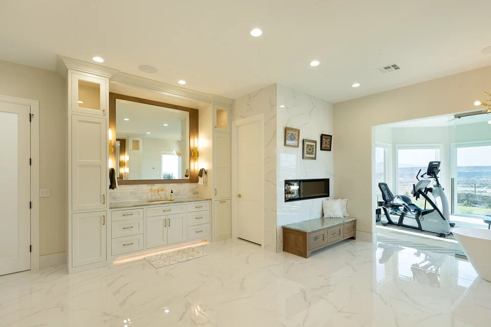Bright bathroom with illuminated vanity mirrors and a wall-mounted television