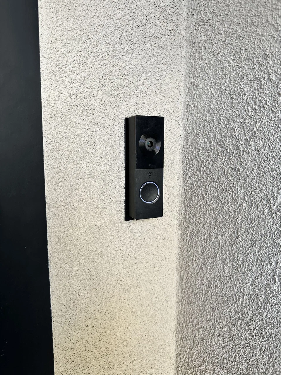 Black video doorbell mounted on an exterior stucco wall