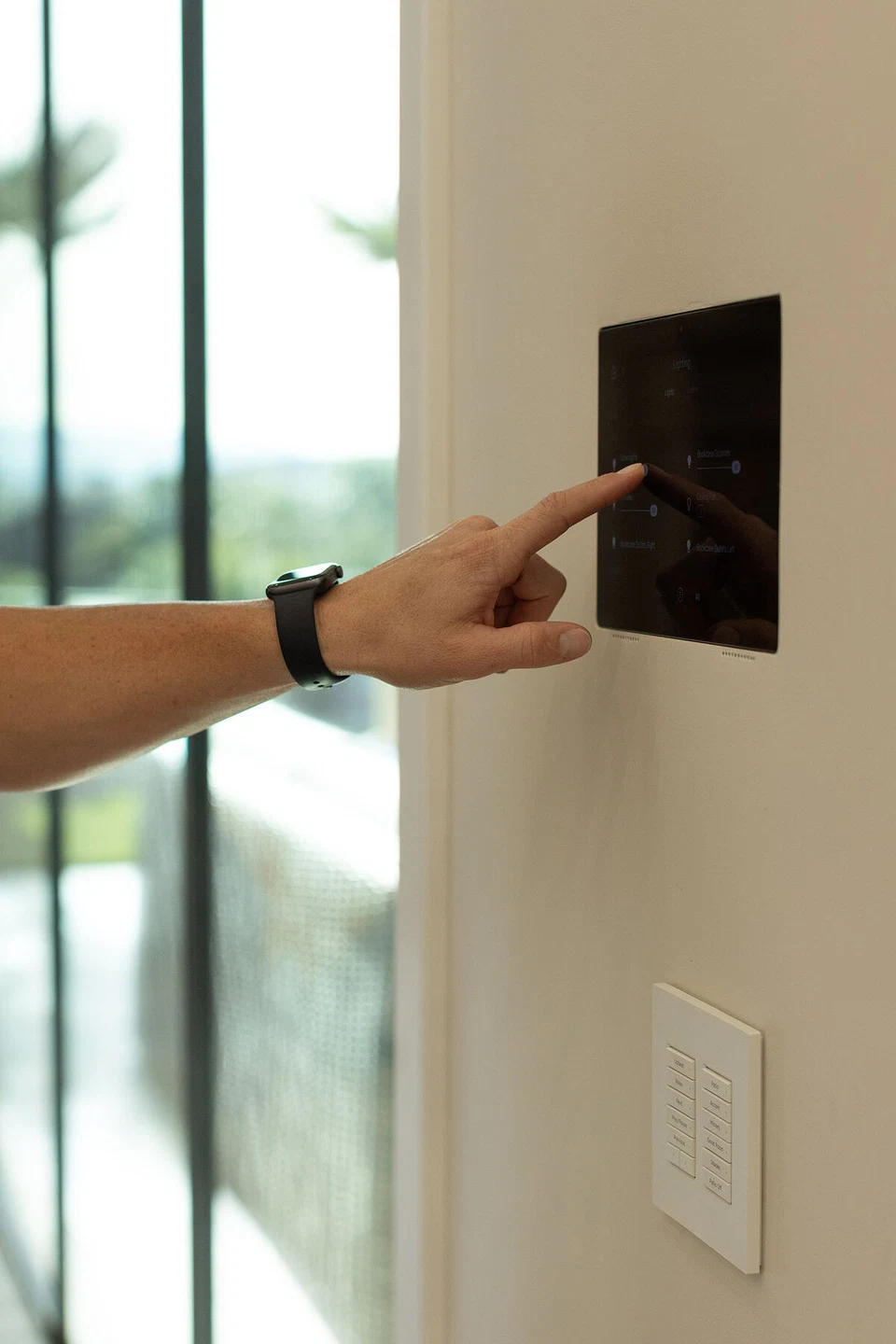 Hand operating a black wall-mounted home-control touchscreen
