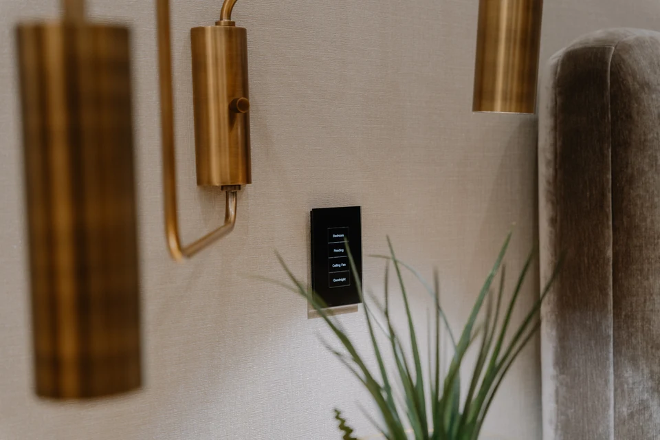 Black wall keypad beneath a brass reading light beside a plant
