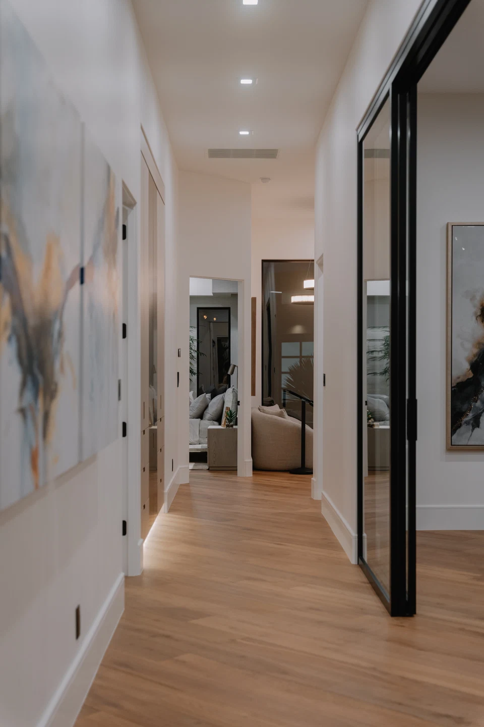 Wood-floored hallway with recessed ceiling lights and framed wall art