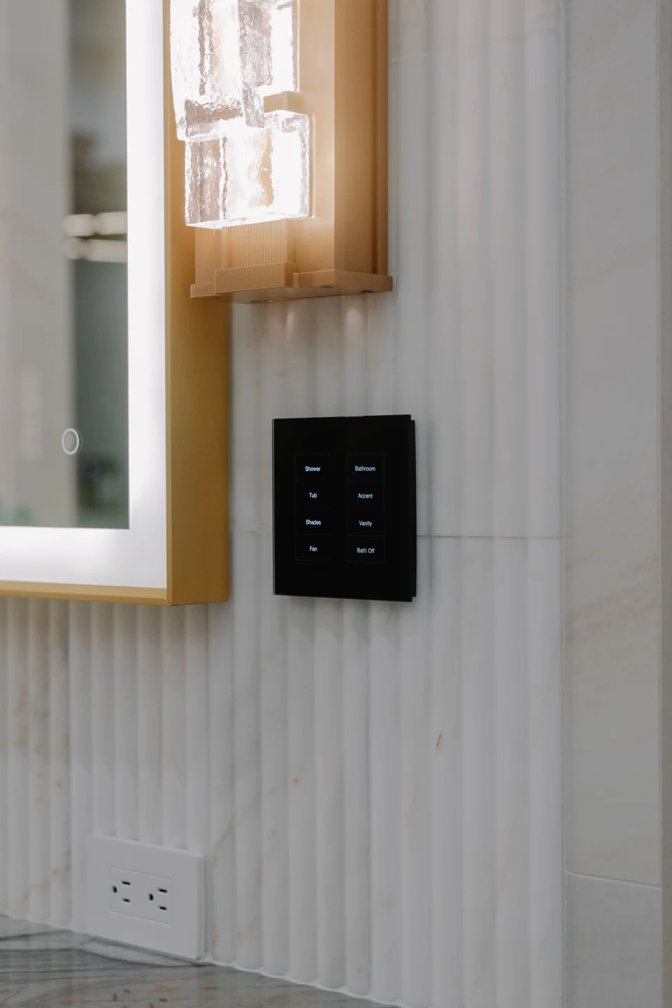 Black bathroom keypad beside a backlit mirror and glass wall sconce