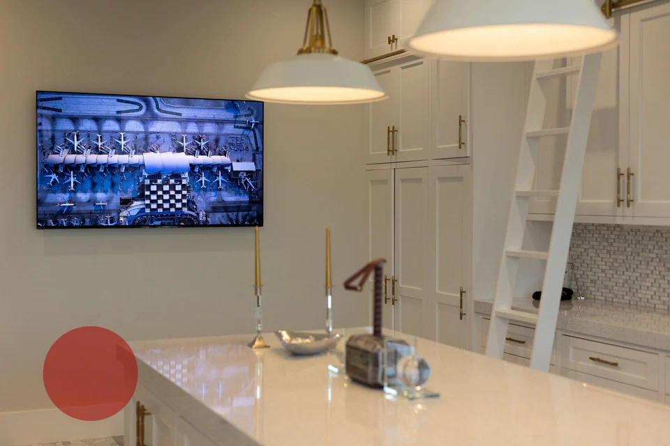 Kitchen television beside white cabinetry and an island beneath pendant lights