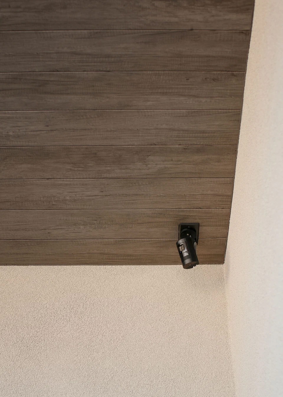 Black exterior security camera beneath a wood patio ceiling