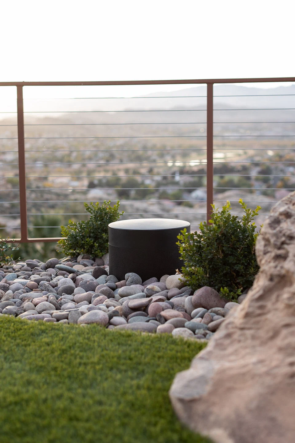 Cylindrical landscape speaker among rocks beside a glass railing