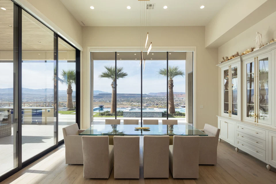 Dining table facing large windows overlooking the pool and palm trees